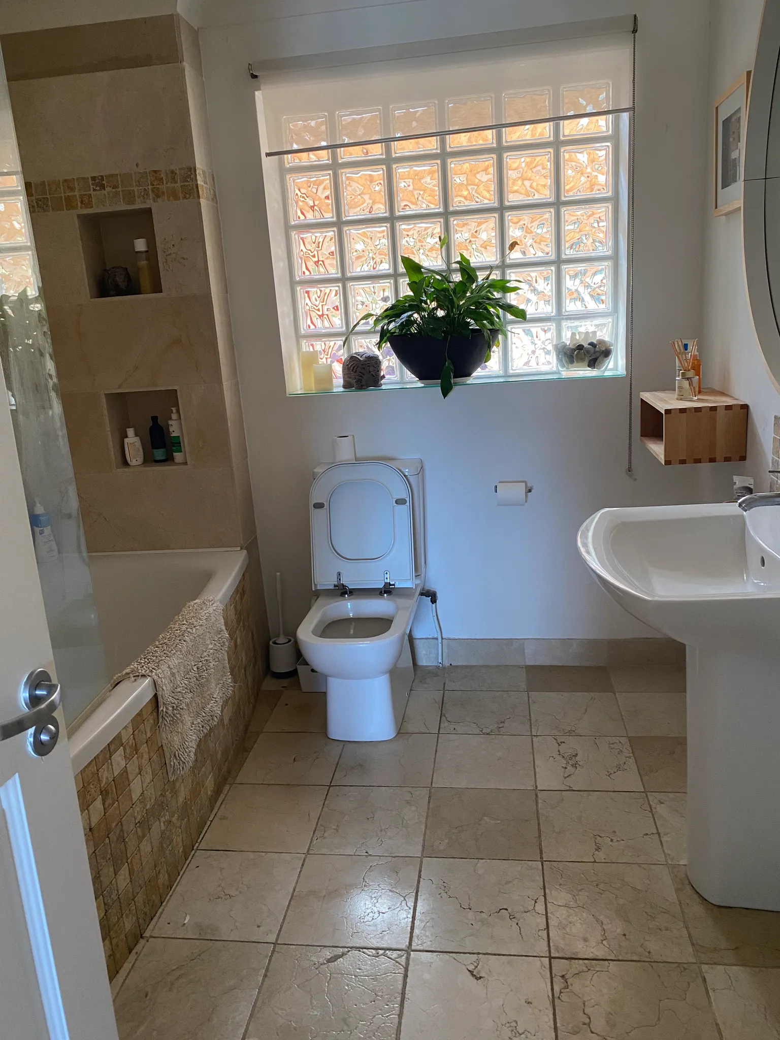 Bathroom with a toilet (lid up), pedestal sink, bathtub with tiled surround, and a glass-block window with a potted plant on the sill.