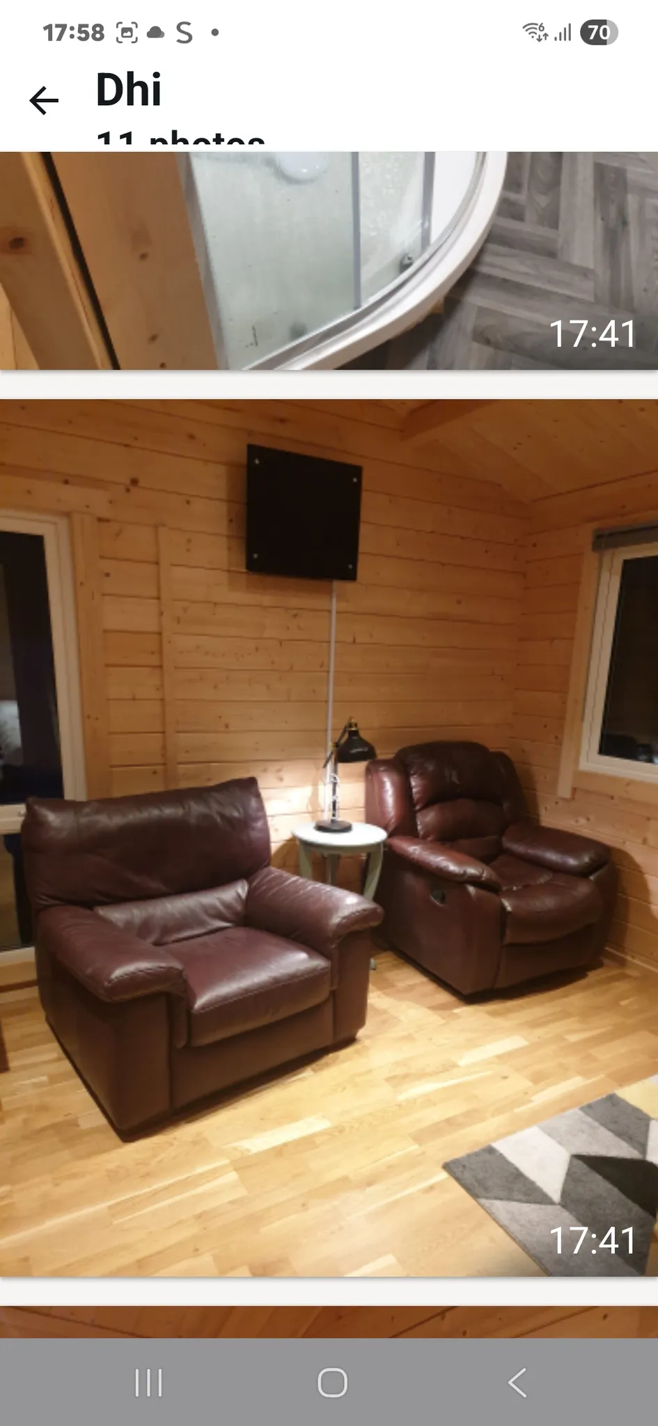 Living room with two brown leather armchairs, a small round side table with a lamp between them, wooden paneled walls and a wall-mounted black square panel. Hardwood floor and part of a rug visible.