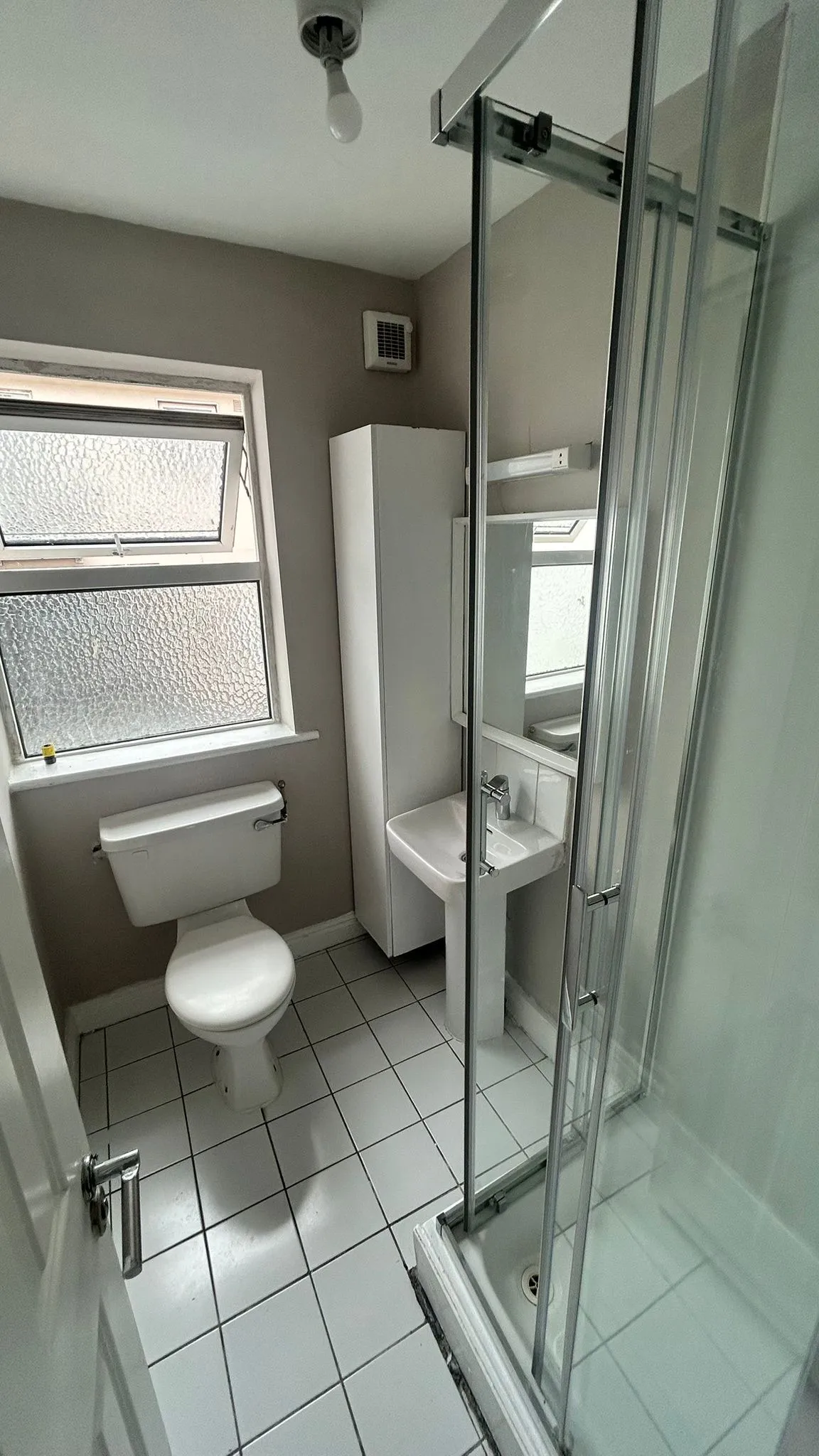 Bathroom with a toilet, pedestal sink, tall storage cabinet, frosted window and a corner shower with sliding glass door.