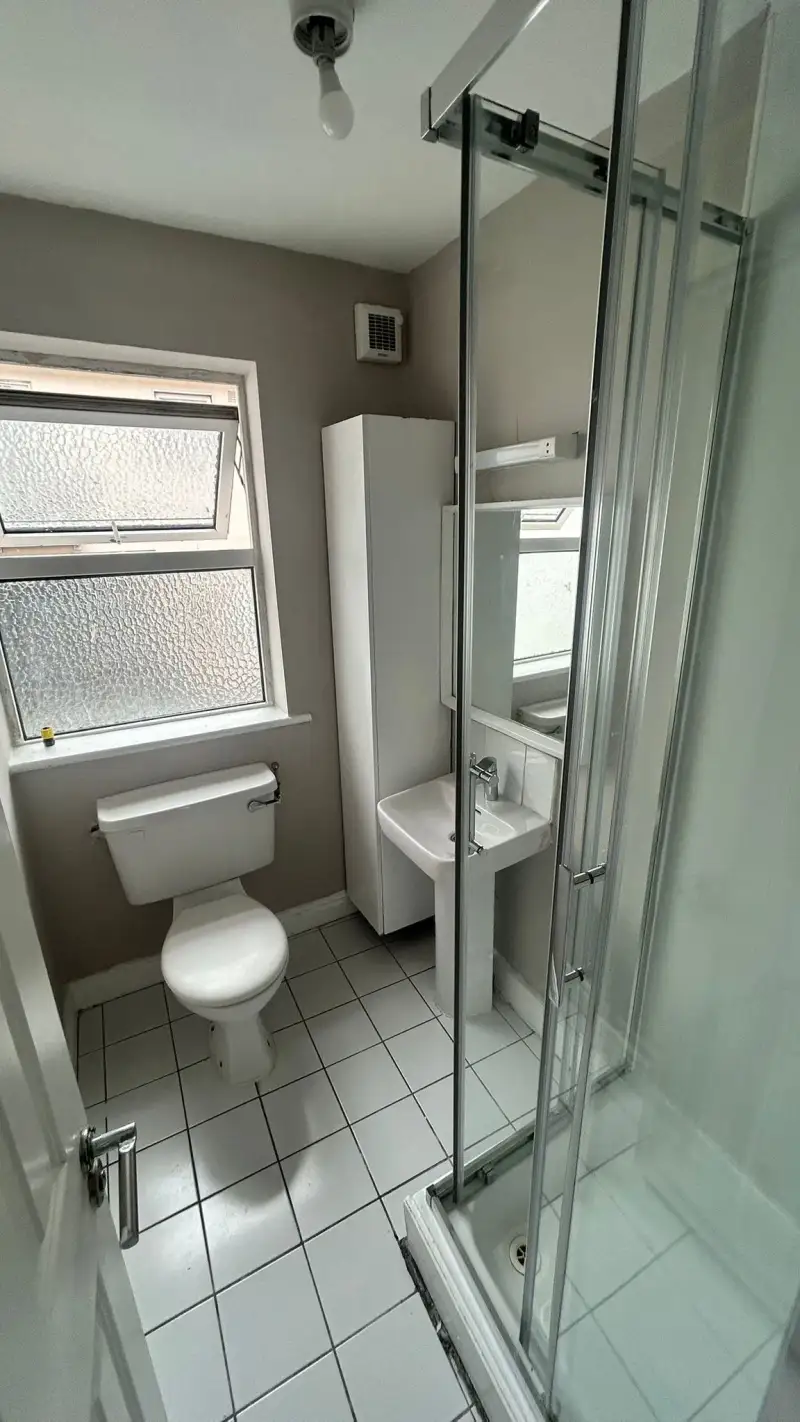 Bathroom with a toilet, pedestal sink, tall storage cabinet, frosted window and a corner shower with sliding glass door.