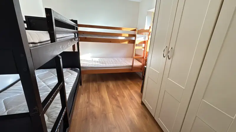 Bedroom with two bunk beds, mattresses, a white wardrobe, and a small window letting in natural light.