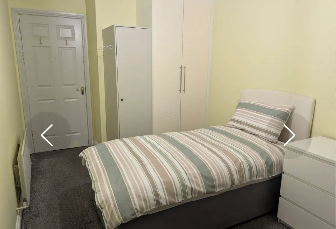 Bedroom with a single bed with striped bedding, a tall wardrobe, a chest of drawers, and a closed door.