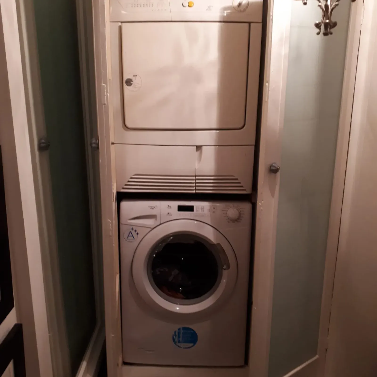Stacked front-loading washing machine and dryer inside a narrow closet with two folding doors partially open