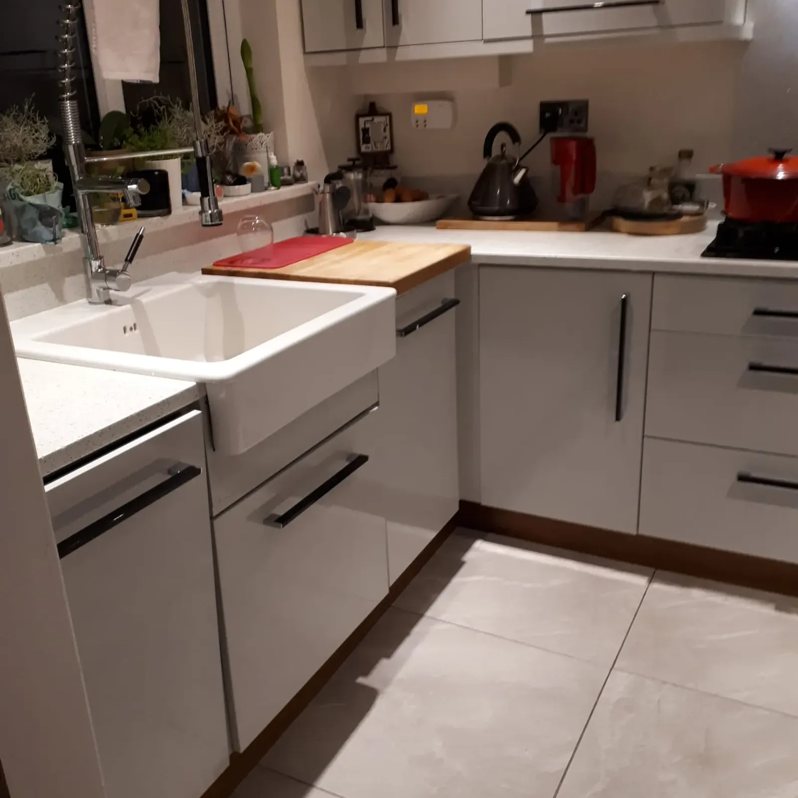 Kitchen corner with a white sink and tall spring faucet, countertop with cutting board, kettle, cabinets and a red pot on the hob