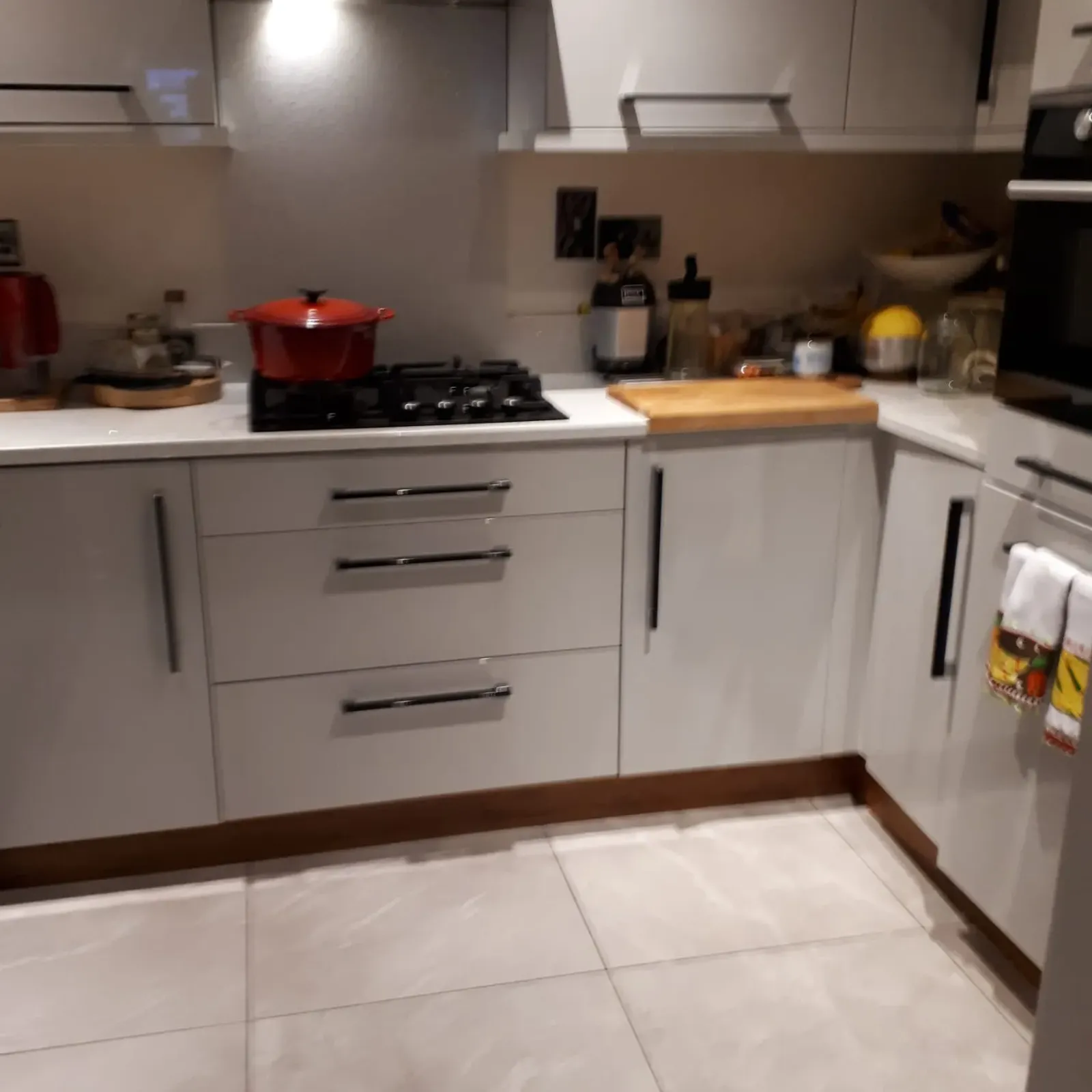 Kitchen with a gas stove and range hood, white cabinets, a red pot on the stovetop and a countertop with a cutting board and small appliances.