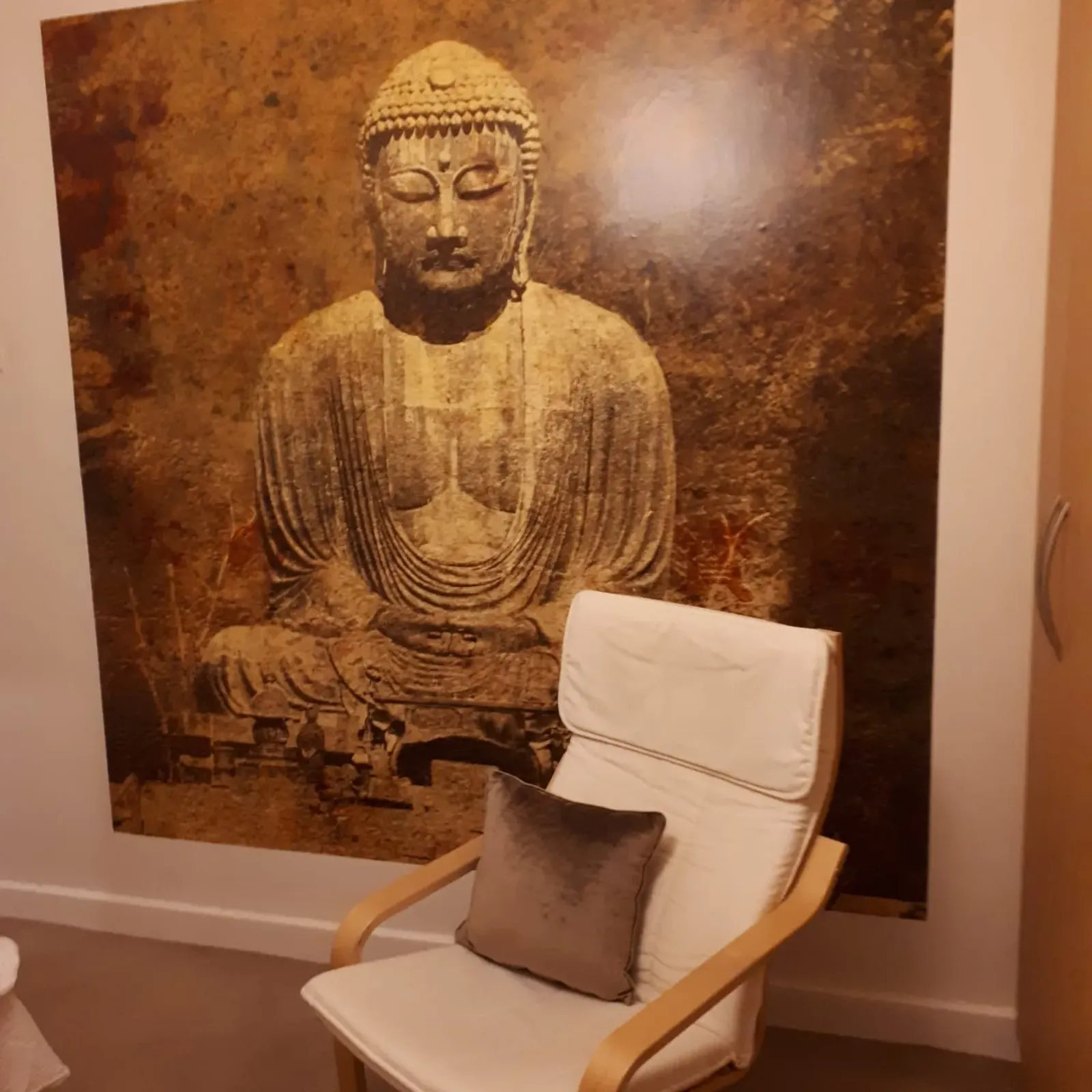 Living room with a white armchair and cushion placed in front of a large Buddha wall mural