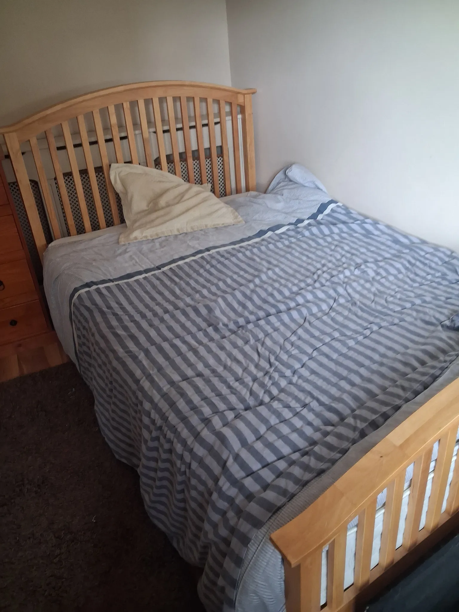 Bedroom with a wooden bed frame, striped duvet and two pillows against a plain wall