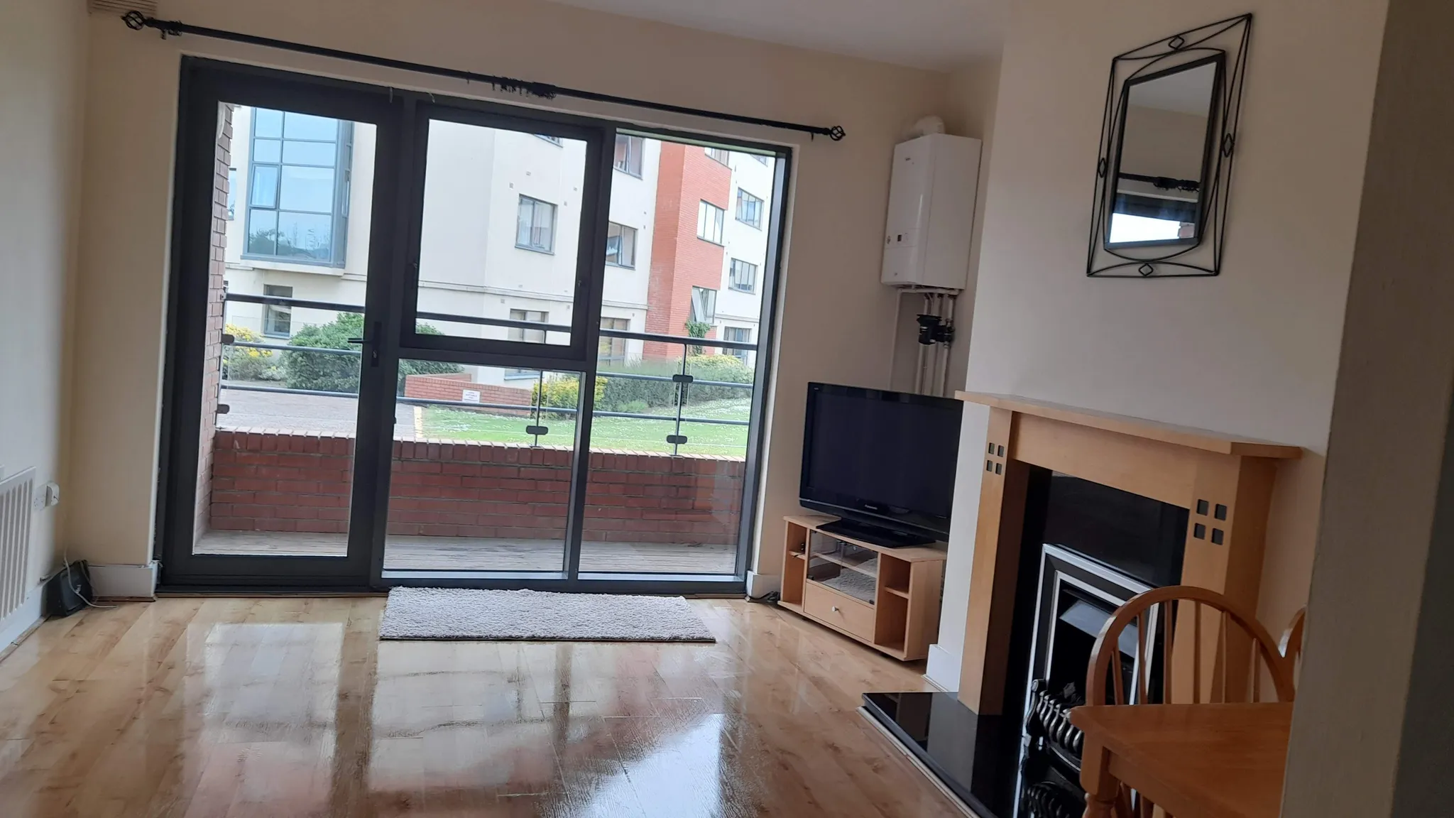 Living room with large sliding glass door leading to a small balcony, hardwood floor, TV on a stand, and a fireplace with a mirror above it.