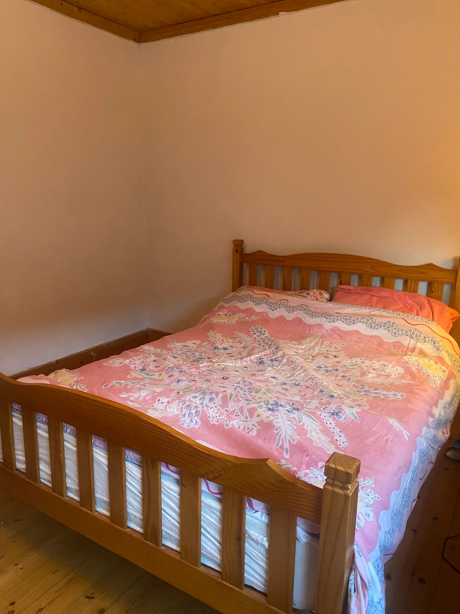 Bedroom with a wooden bed frame and pink bedding against a plain wall