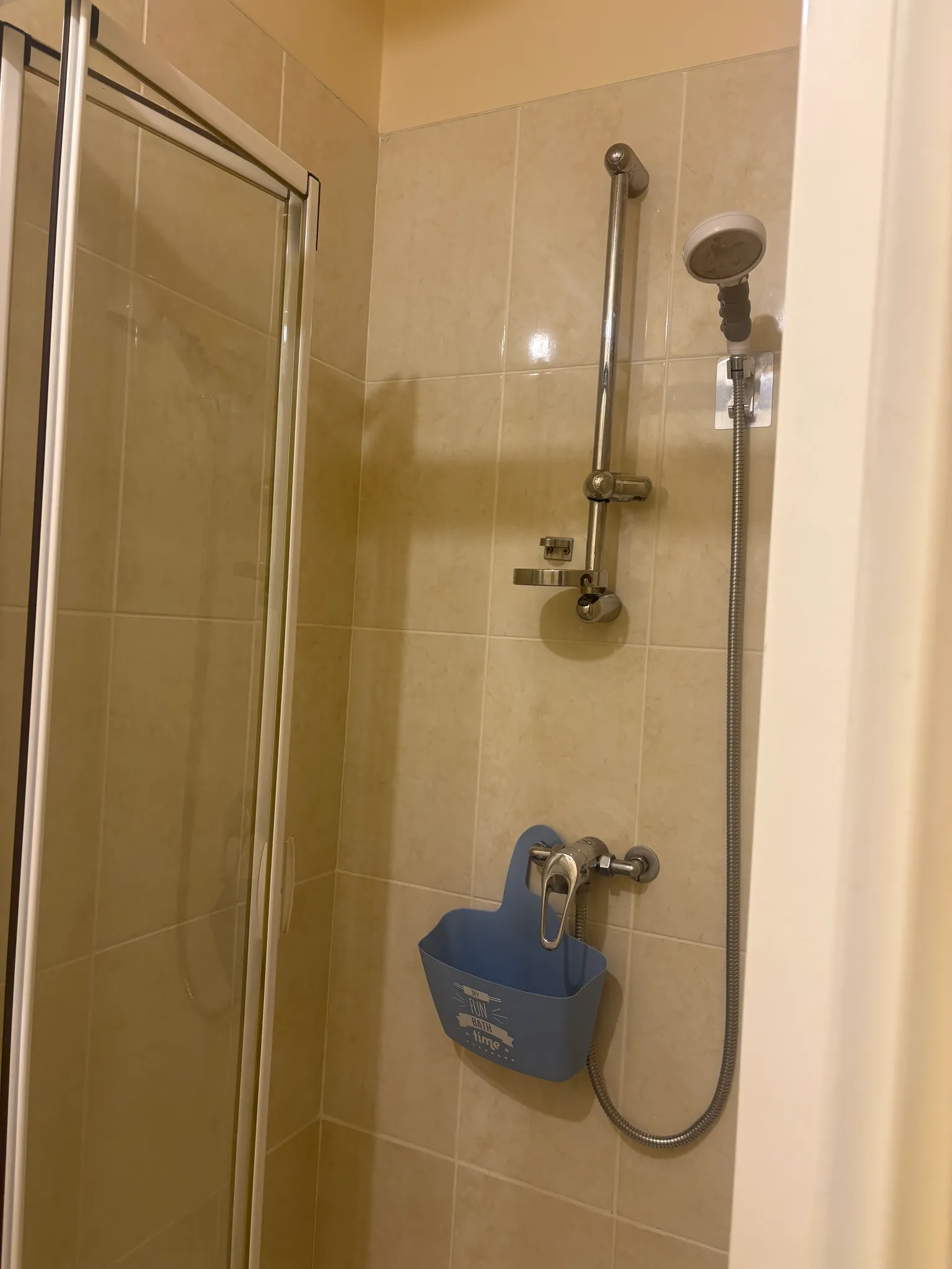 Bathroom shower stall with tiled walls, sliding glass door, adjustable handheld showerhead and faucet with a blue hanging toiletry caddy.
