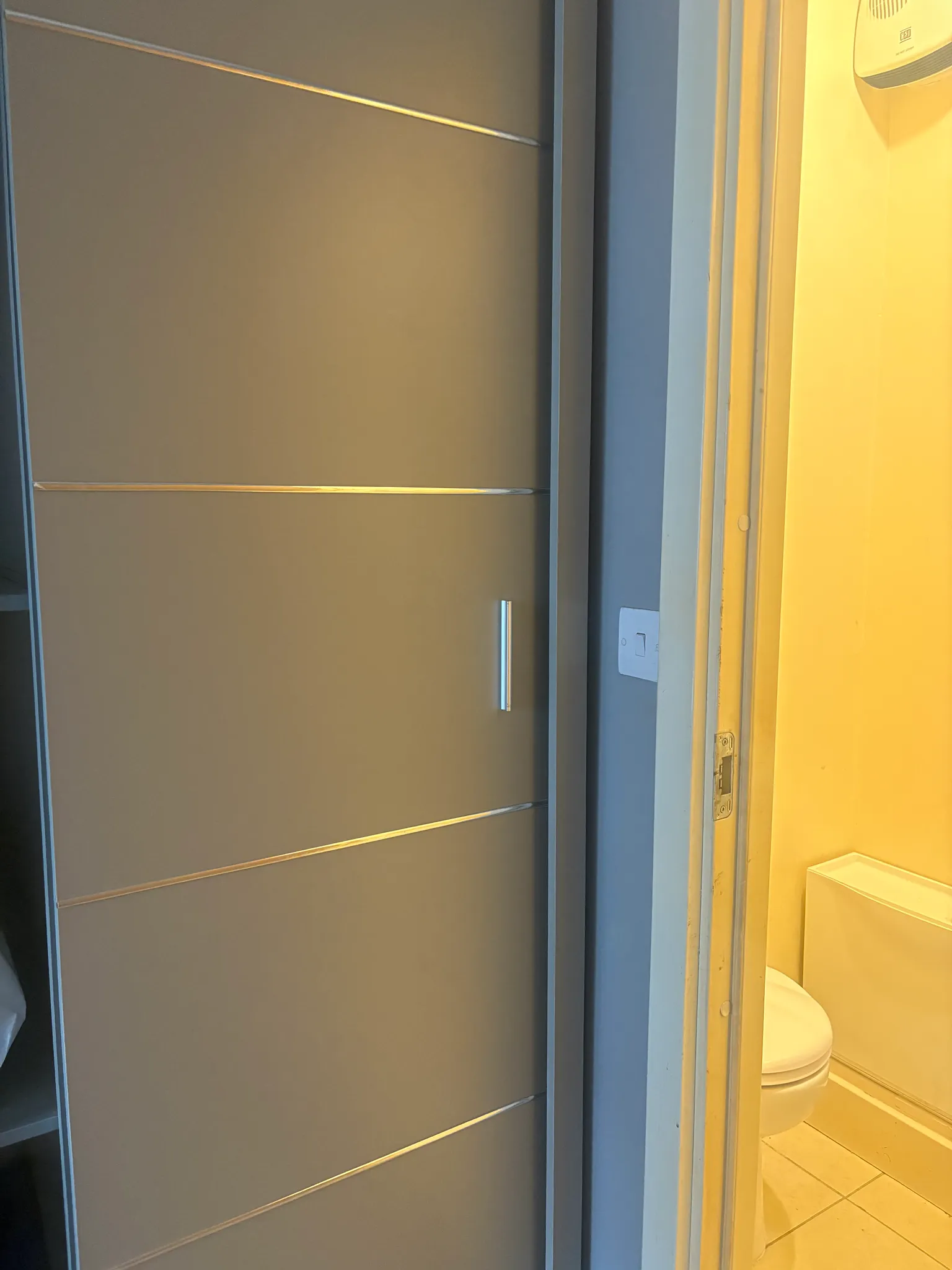 Partial view of a sliding closet door next to a doorway showing a bathroom with a toilet and sink corner.