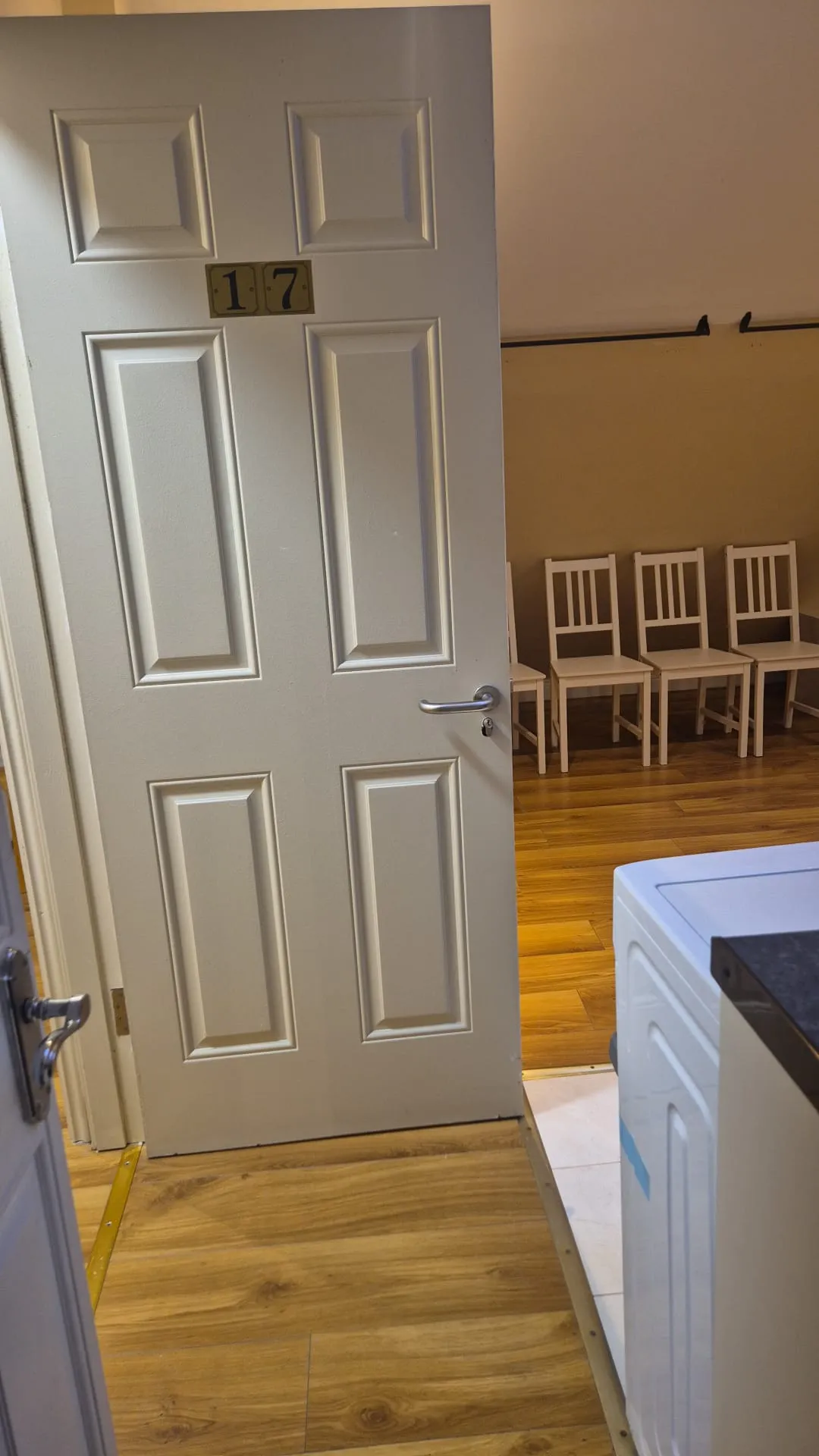 Partially open interior door labeled 17 leading to a room with a row of wooden chairs and wood flooring.