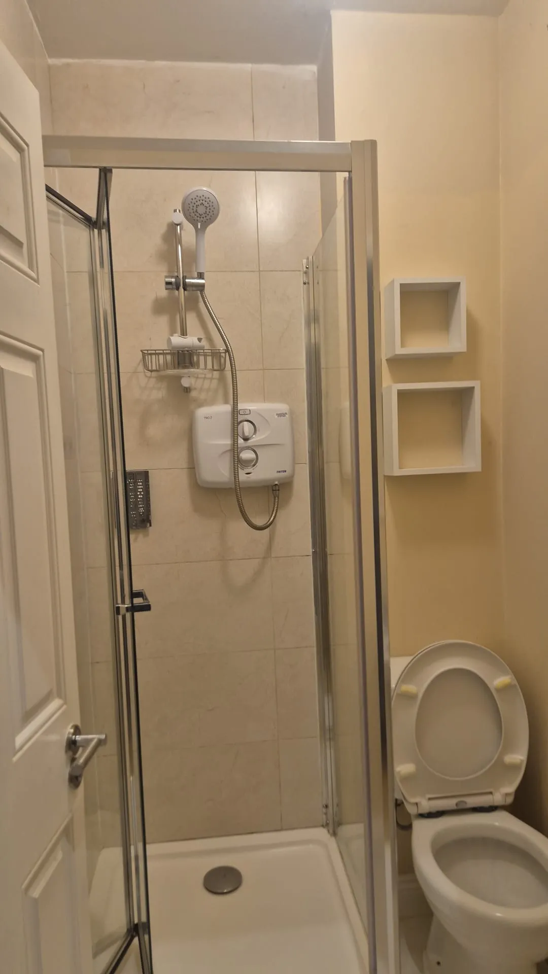 Bathroom with a glass-enclosed shower stall, wall-mounted shower unit and handheld showerhead, and a toilet with the seat up.
