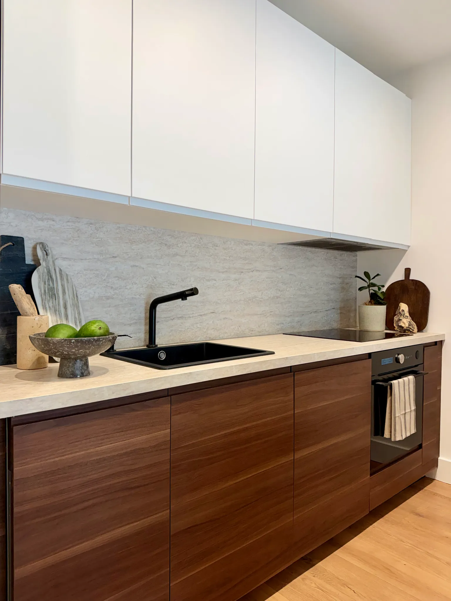 Kitchen countertop with a black sink and faucet, white upper cabinets, wooden lower cabinets, and a stovetop with oven