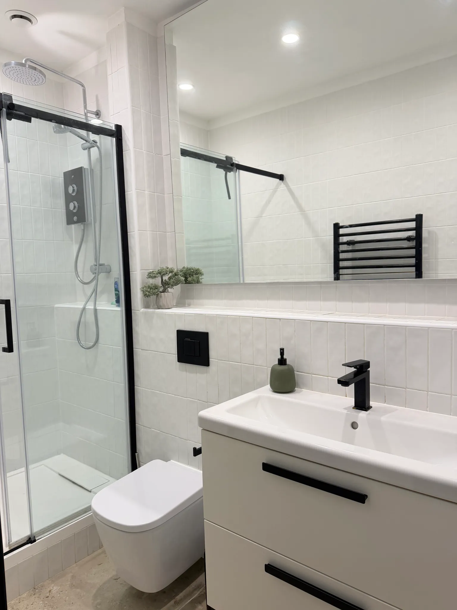Bathroom with a glass-enclosed shower, wall-mounted showerhead, toilet, sink with black faucet, large mirror and tiled walls.