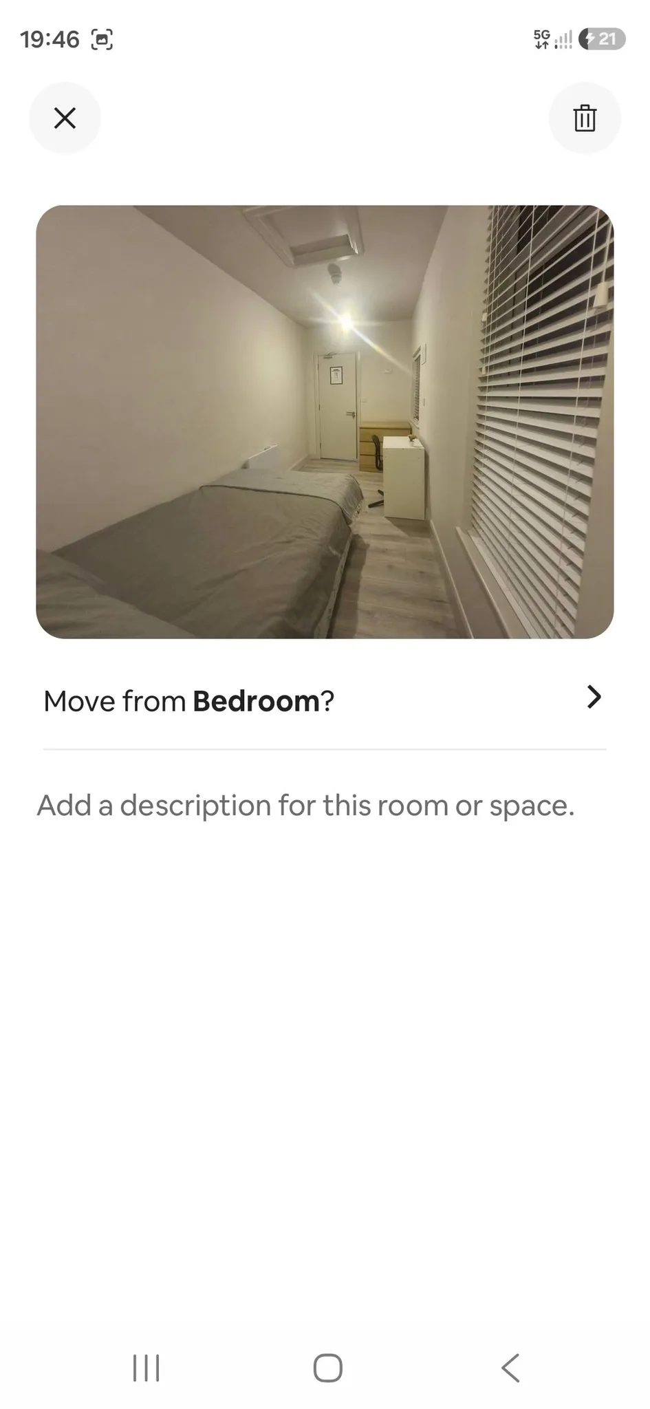 Narrow bedroom with a single bed along the left wall, a window with blinds on the right, and a small desk and chair near the far door.