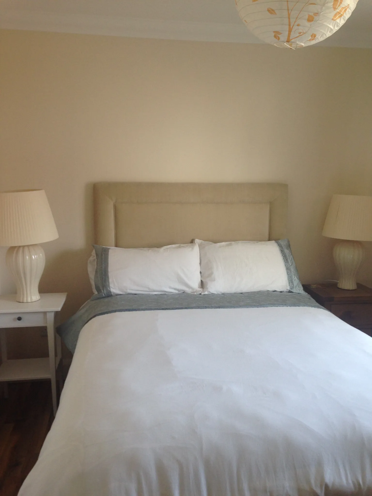 Bedroom with a bed and upholstered headboard, two bedside lamps, pillows and a duvet.