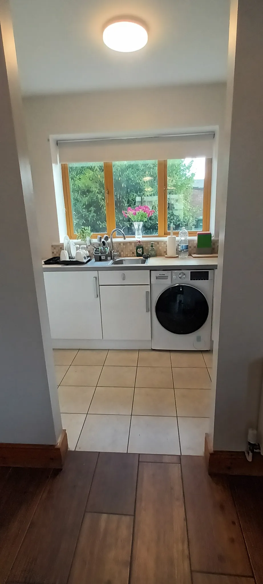 Kitchen with a sink and countertop under a three-pane window, white cabinets and a front-loading washer to the right.