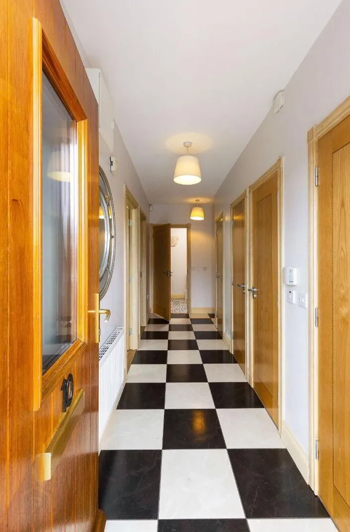 Long interior hallway with black-and-white checkered floor, wooden doors on both sides, pendant ceiling lights, and a partially open door at the far end.