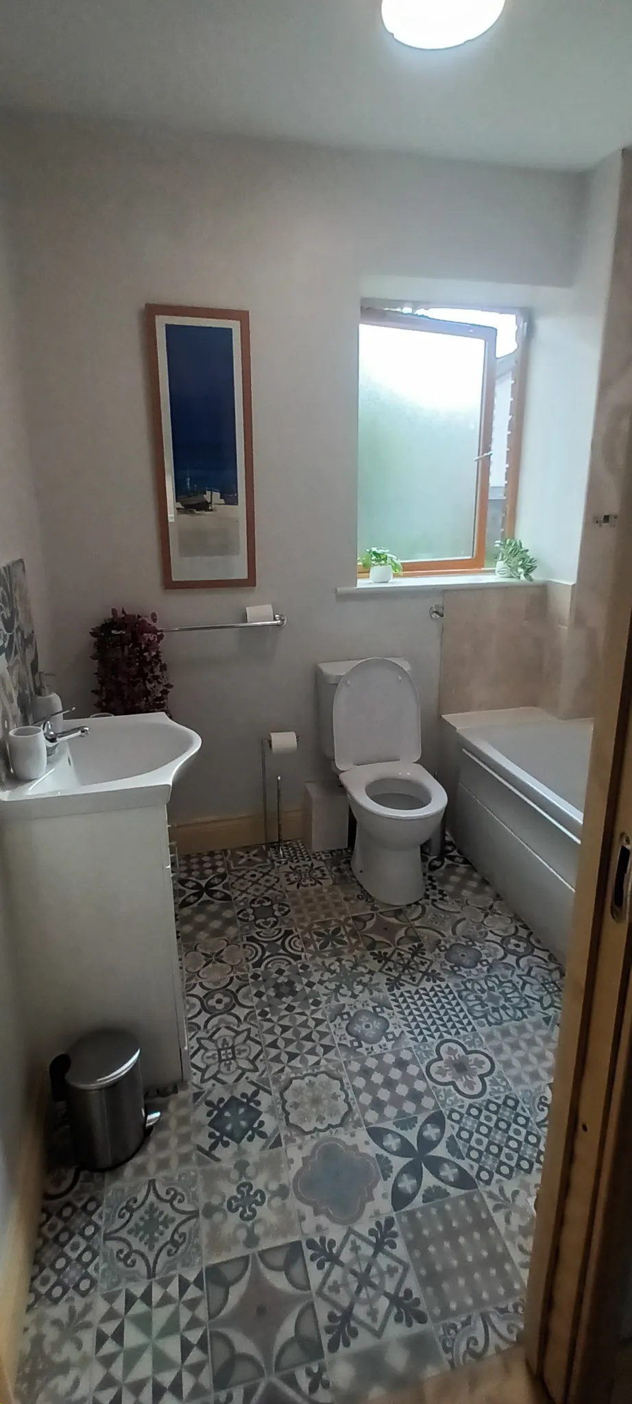 Bathroom with a toilet, sink vanity, bathtub, patterned tile floor and a frosted window with small potted plants on the sill.