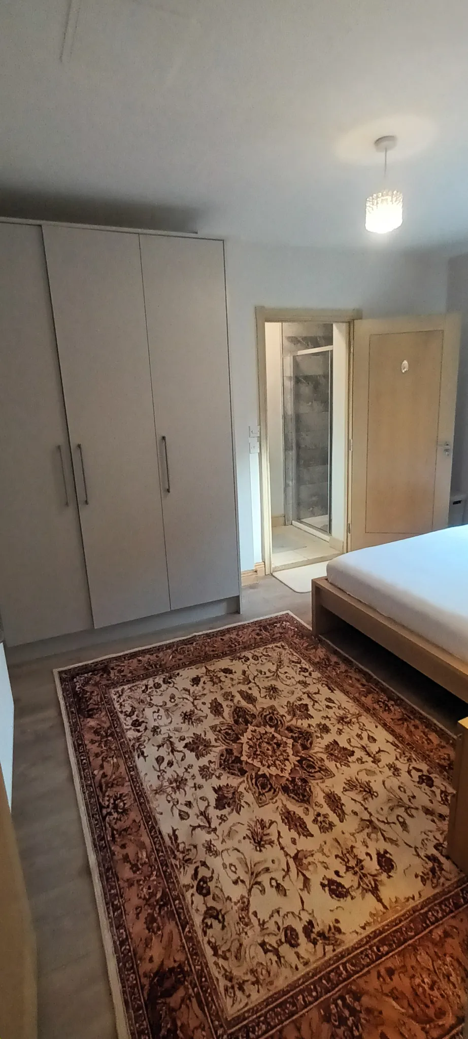 Bedroom with a double bed frame, large wardrobe, patterned area rug and an open door leading to a small en-suite shower area.