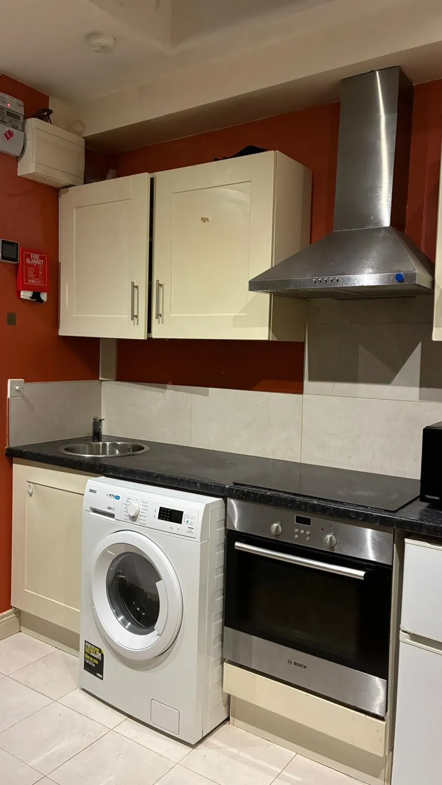 Kitchen with countertop, wall cabinets, stainless steel extractor hood, built-in oven, front-loading washing machine and small sink.