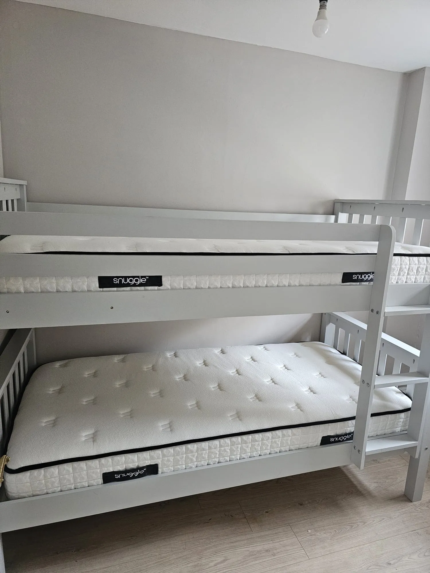 Bedroom with a white wooden bunk bed, two mattresses and a ladder against a plain light-colored wall
