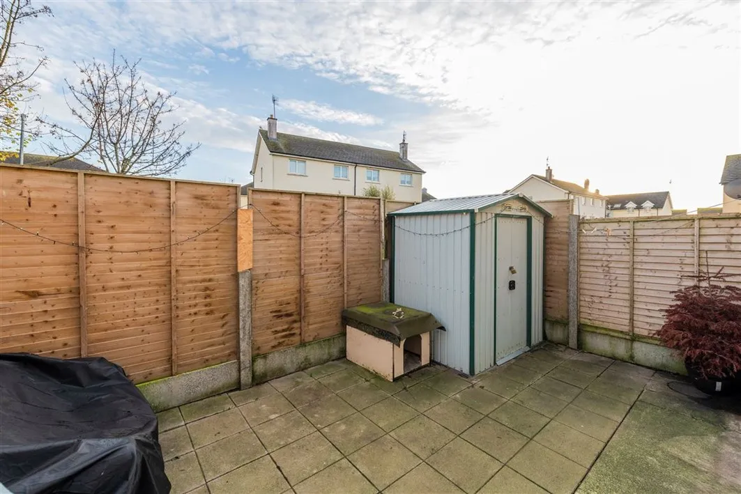 Small paved backyard with wooden fence, metal storage shed and small dog house.