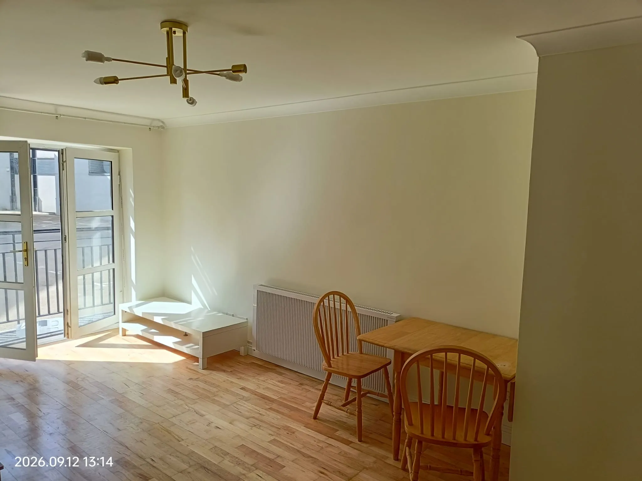 Living room with glass balcony doors, wooden floor, small white coffee table, radiator and a wooden dining table with chairs.