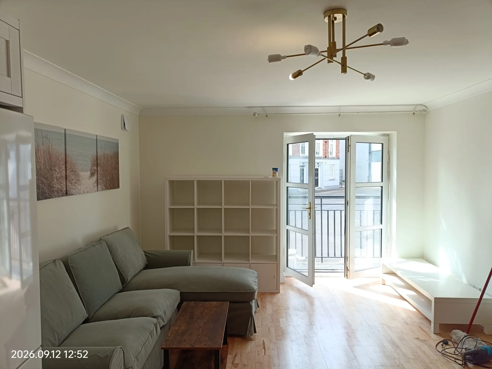 Living room with a green upholstered sofa, low wooden coffee table, cube shelving unit and French doors opening to a small balcony.