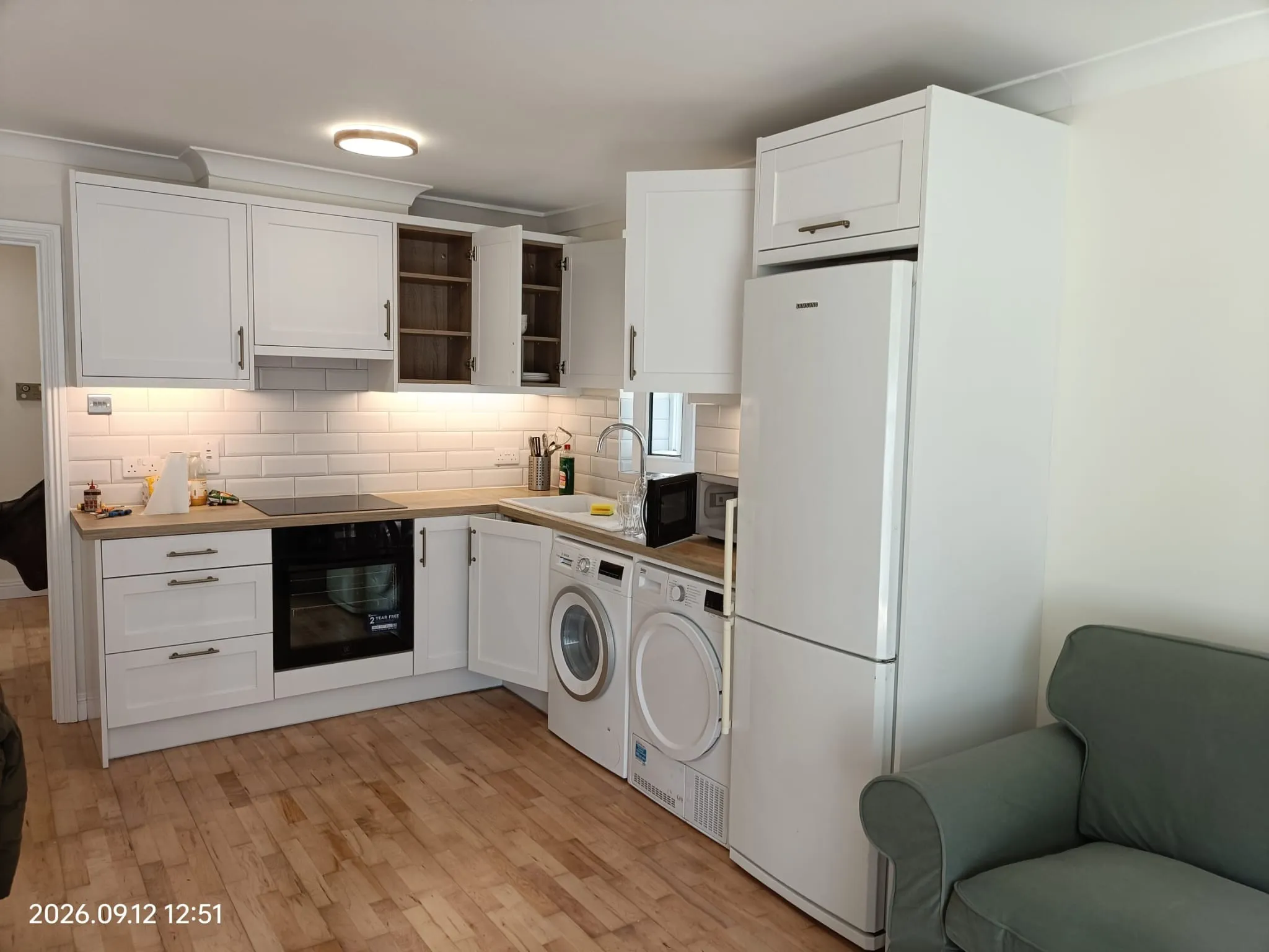 Kitchen with white cabinets, refrigerator, oven, stacked washer and dryer, countertop sink and open upper cabinet doors.