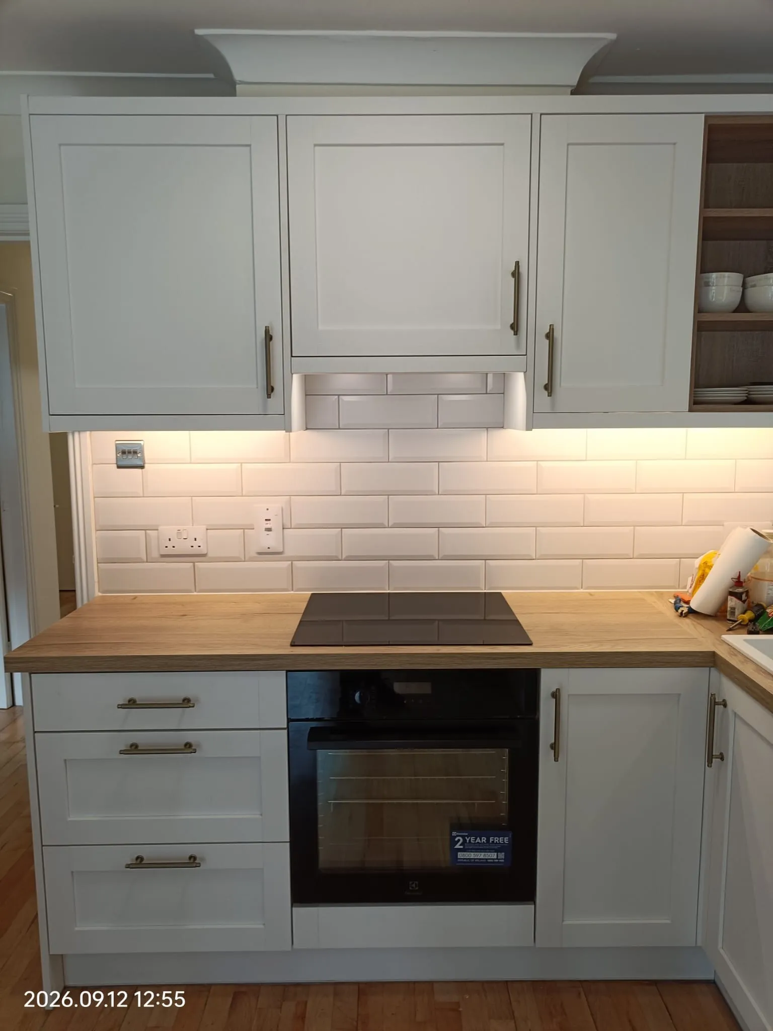 Kitchen counter with an induction cooktop, built-in oven, white upper cabinets and subway-tile backsplash with under-cabinet lighting.