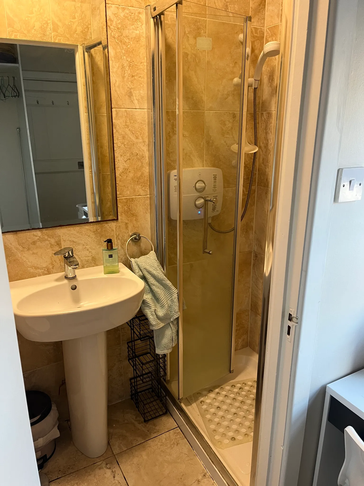 Bathroom with a pedestal sink, mirror, soap dispenser, towel, and a corner shower with glass door and handheld showerhead.