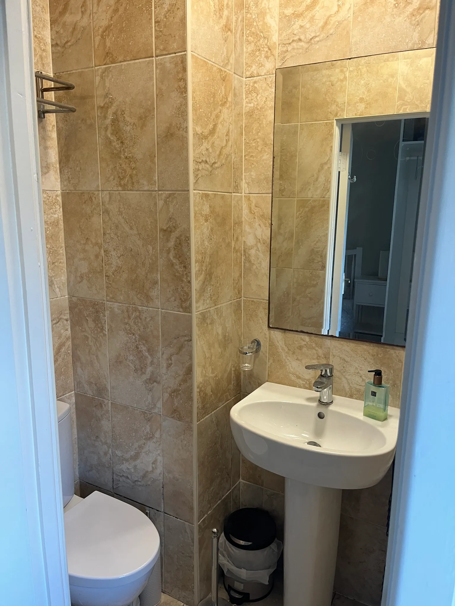 Small bathroom with tiled walls, a pedestal sink with soap dispenser, a mirror, and a toilet.