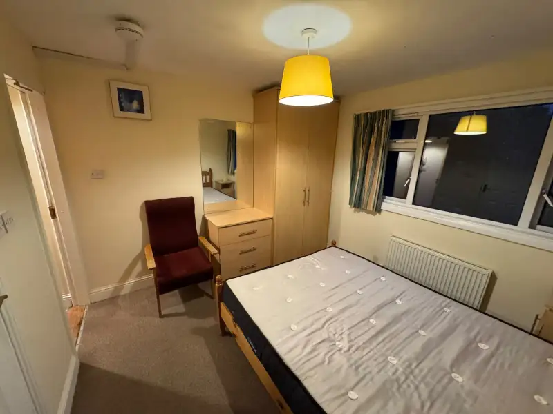 Bedroom with a single bed, wardrobe, chest of drawers with mirror, armchair, window with curtains and a radiator.