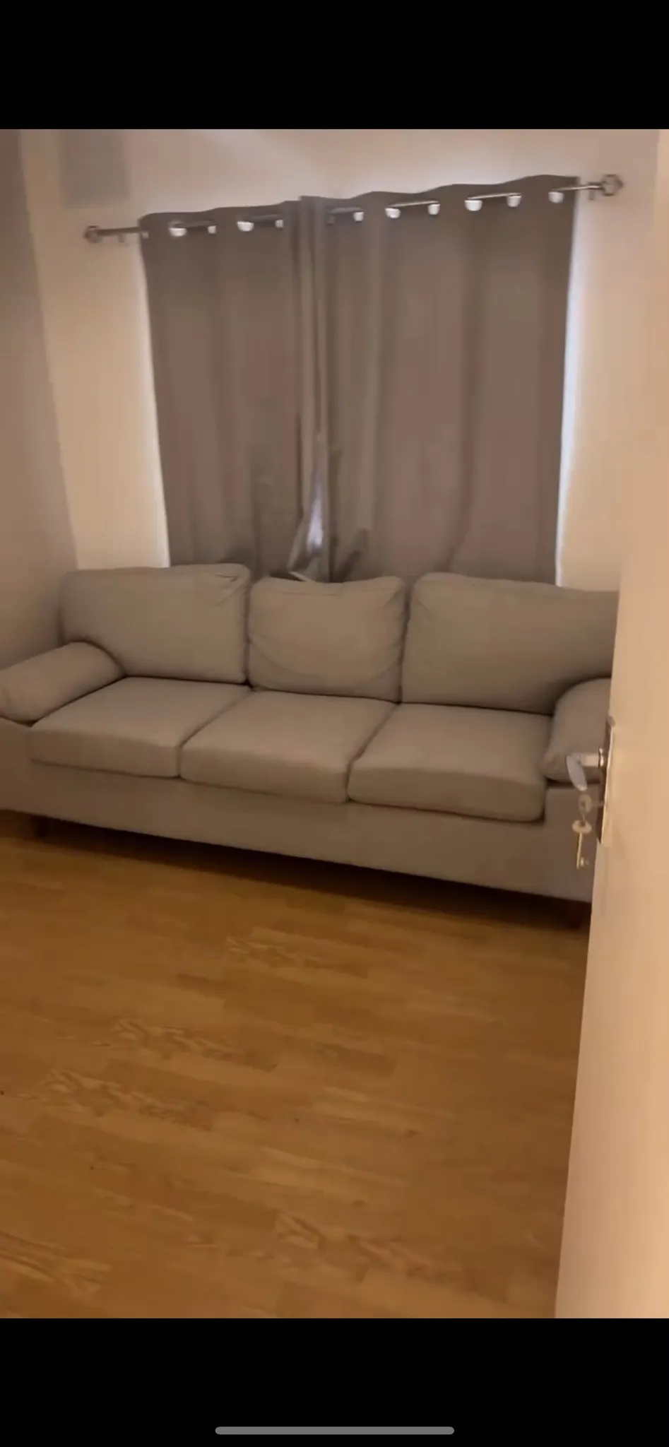 Living room with a three-seat sofa in front of a curtained window and a visible door handle at right