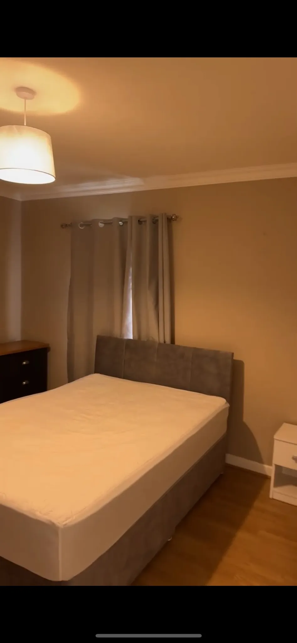Bedroom with a double bed and upholstered headboard, window with closed curtains, bedside table, chest of drawers and ceiling light.