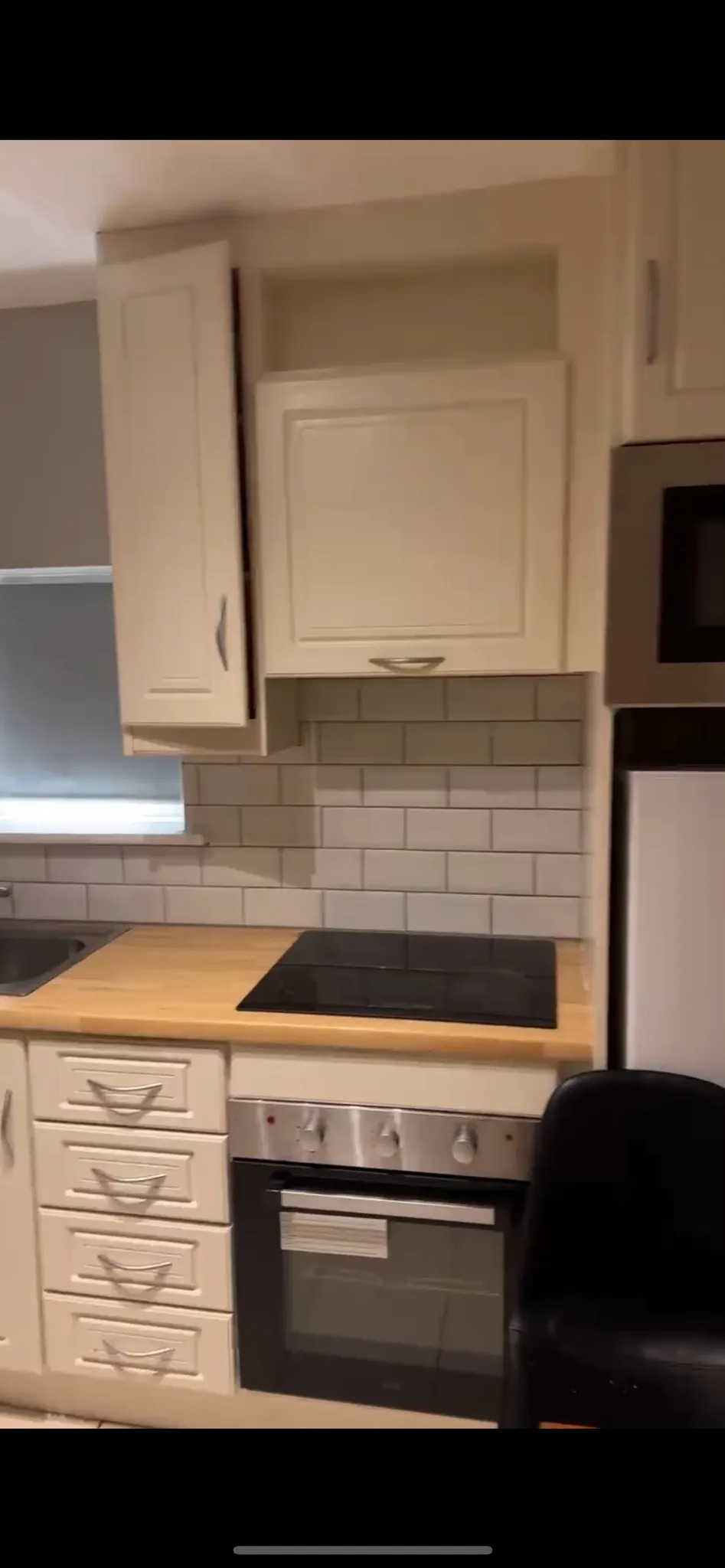 Kitchen countertop with electric cooktop, oven below, white cabinets and subway-tile backsplash