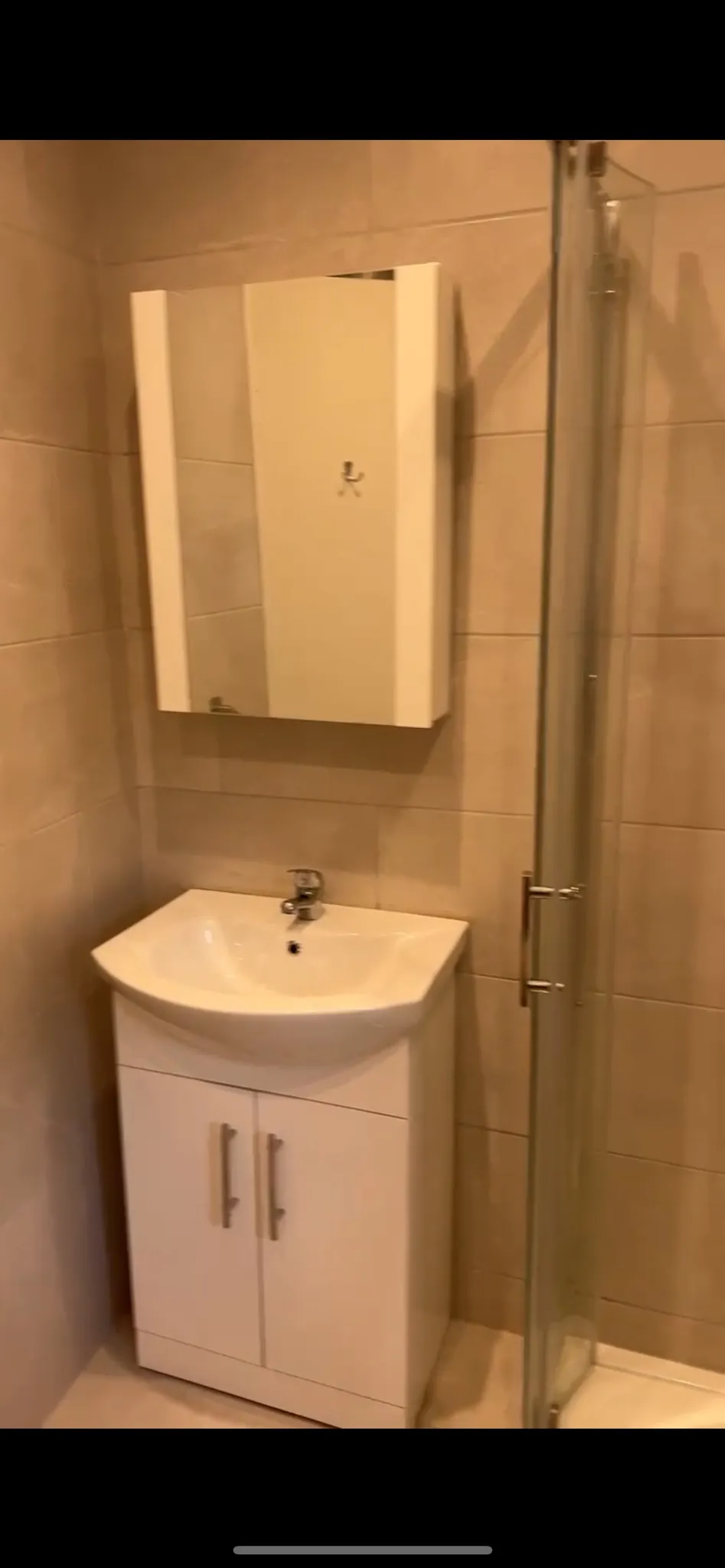 Bathroom with a wall-mounted mirrored cabinet above a white sink vanity and a glass shower door to the right