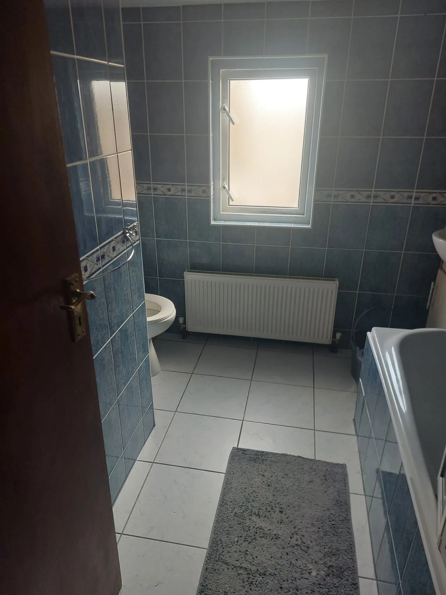 Bathroom with tiled walls, a frosted window, radiator, toilet partially visible and a bathtub at right