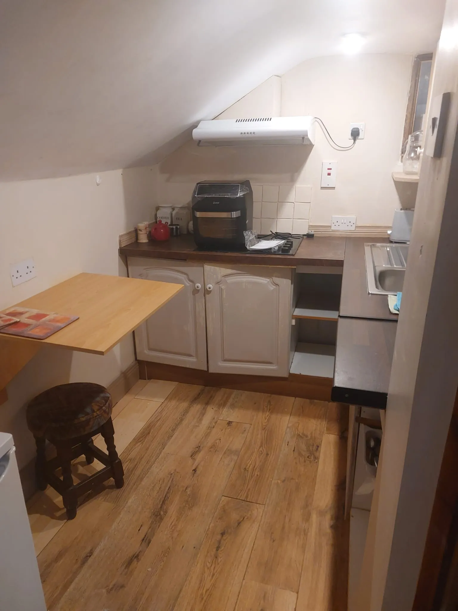 Small kitchen with a countertop oven, extractor hood, sink, cabinets and a fold-down wooden table under a sloped ceiling.