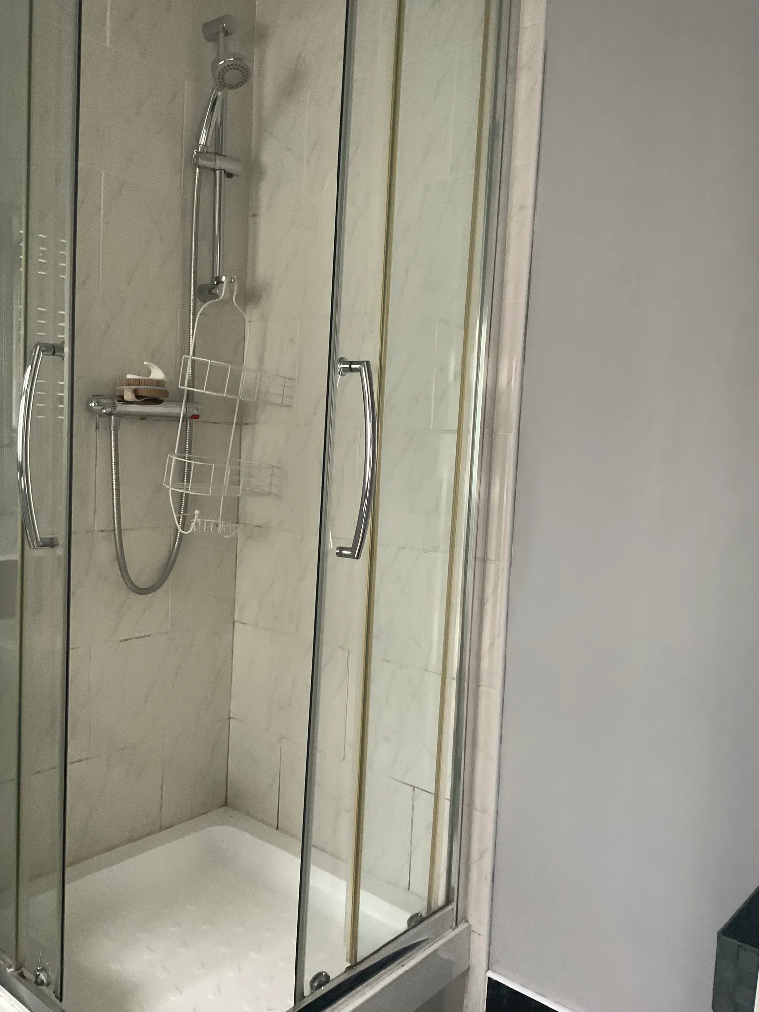 Bathroom shower stall with glass sliding doors, handheld shower head, metal shower caddy and tiled walls above a bathtub base.