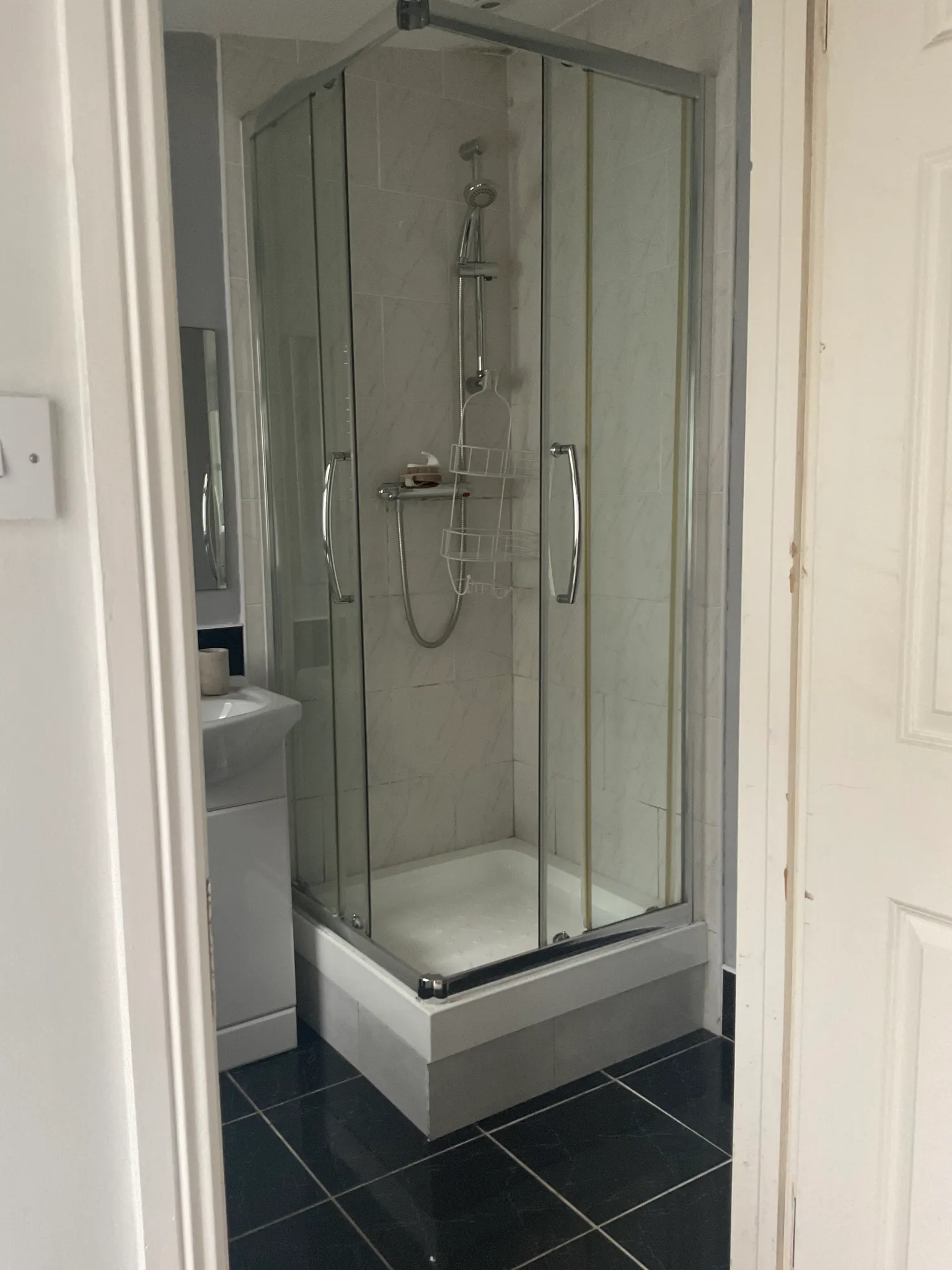 Bathroom with a glass-enclosed corner shower with sliding doors and a hand shower; partial sink visible.