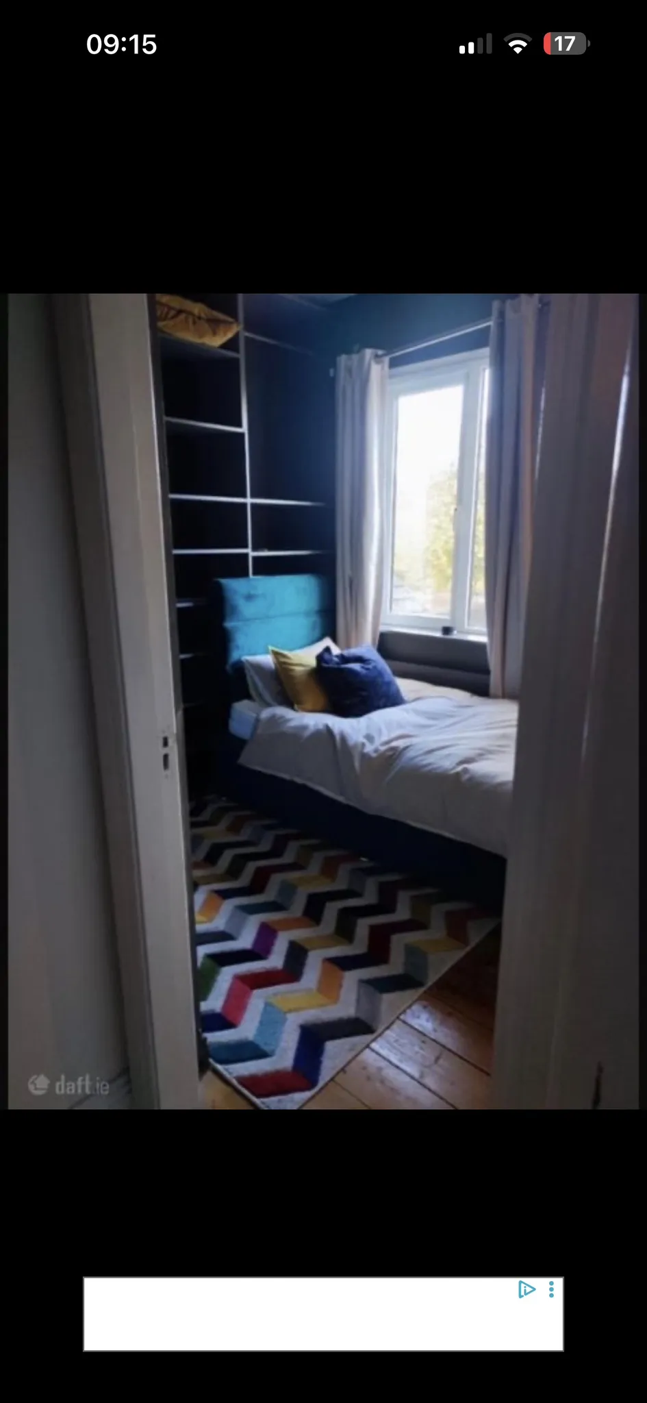 Bedroom with a single bed next to a window, curtains, built-in shelving, a patterned rug, and decorative pillows.