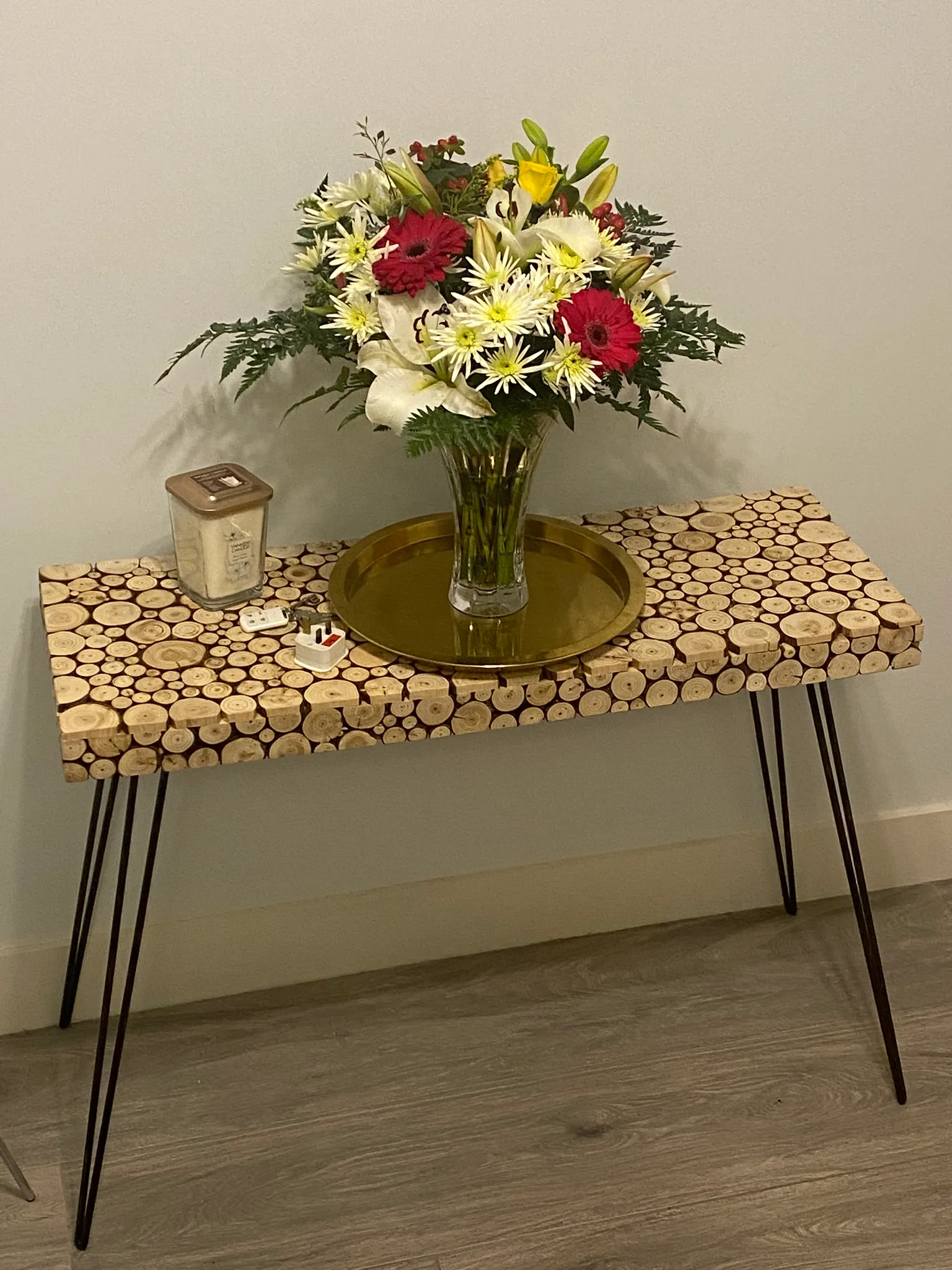 Console table with a vase of mixed flowers on a gold tray against a plain wall