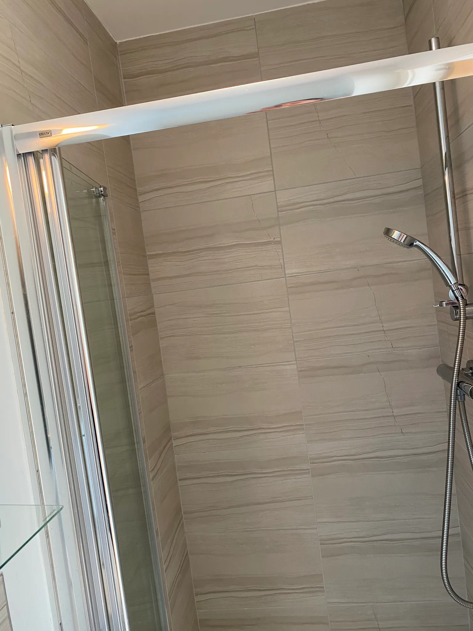 Bathroom shower area with tiled walls, sliding glass door frame and a handheld chrome shower head