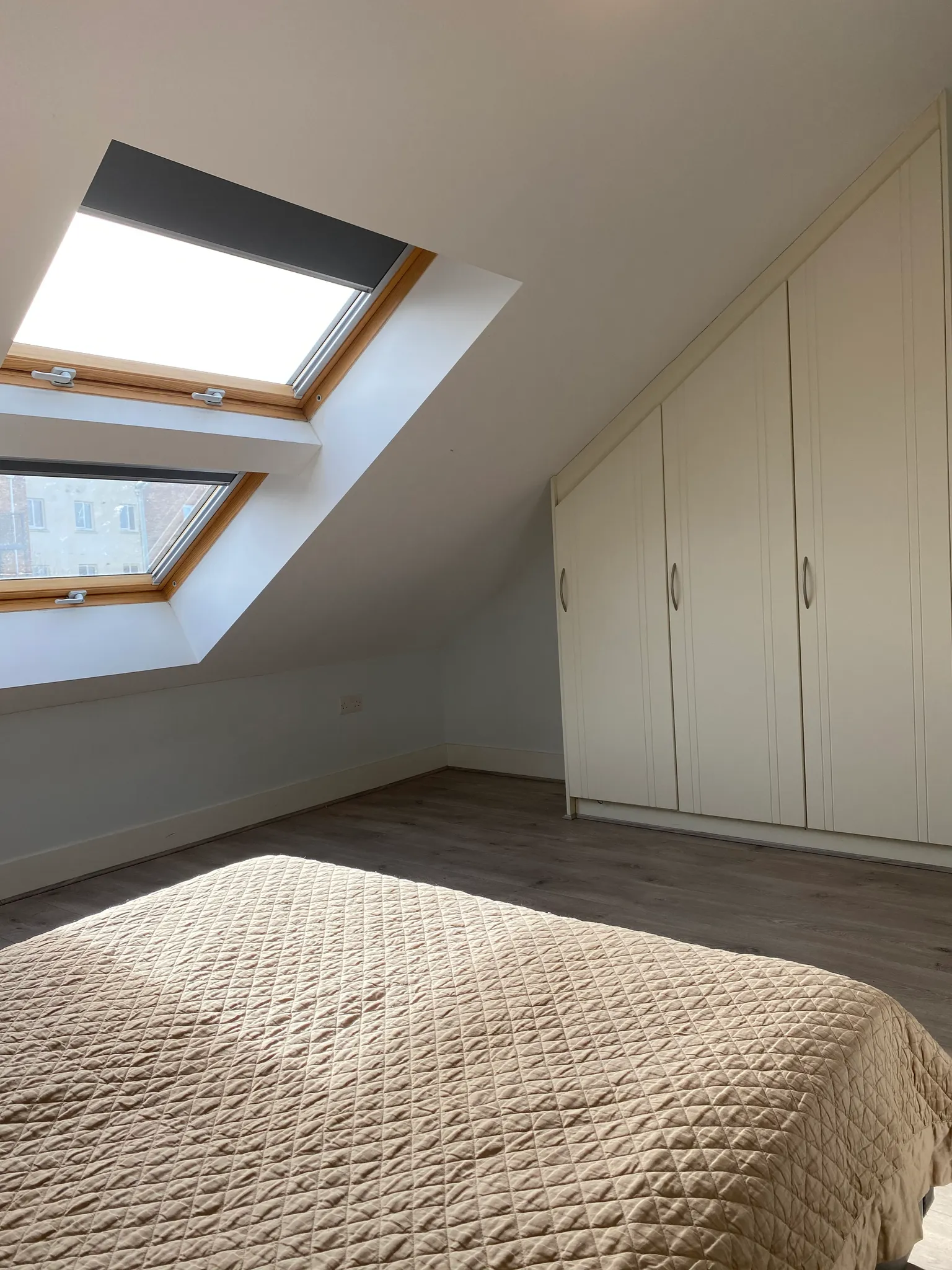 Bedroom with a quilted bed in the foreground, sloped ceiling with two skylight windows, and built-in wardrobes along the right wall