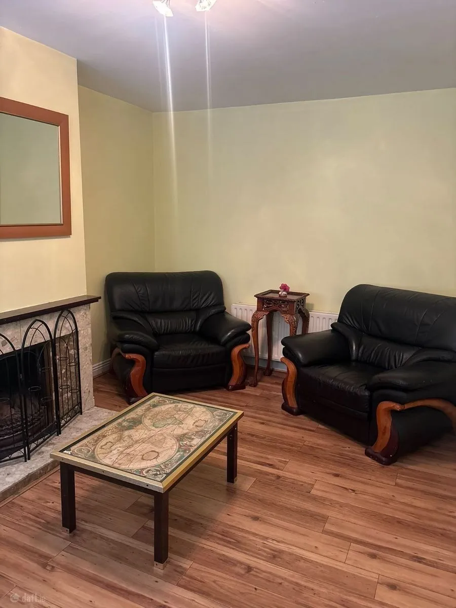 Living room with two black leather armchairs, a low coffee table, fireplace with screen, wall mirror, and wooden floor.