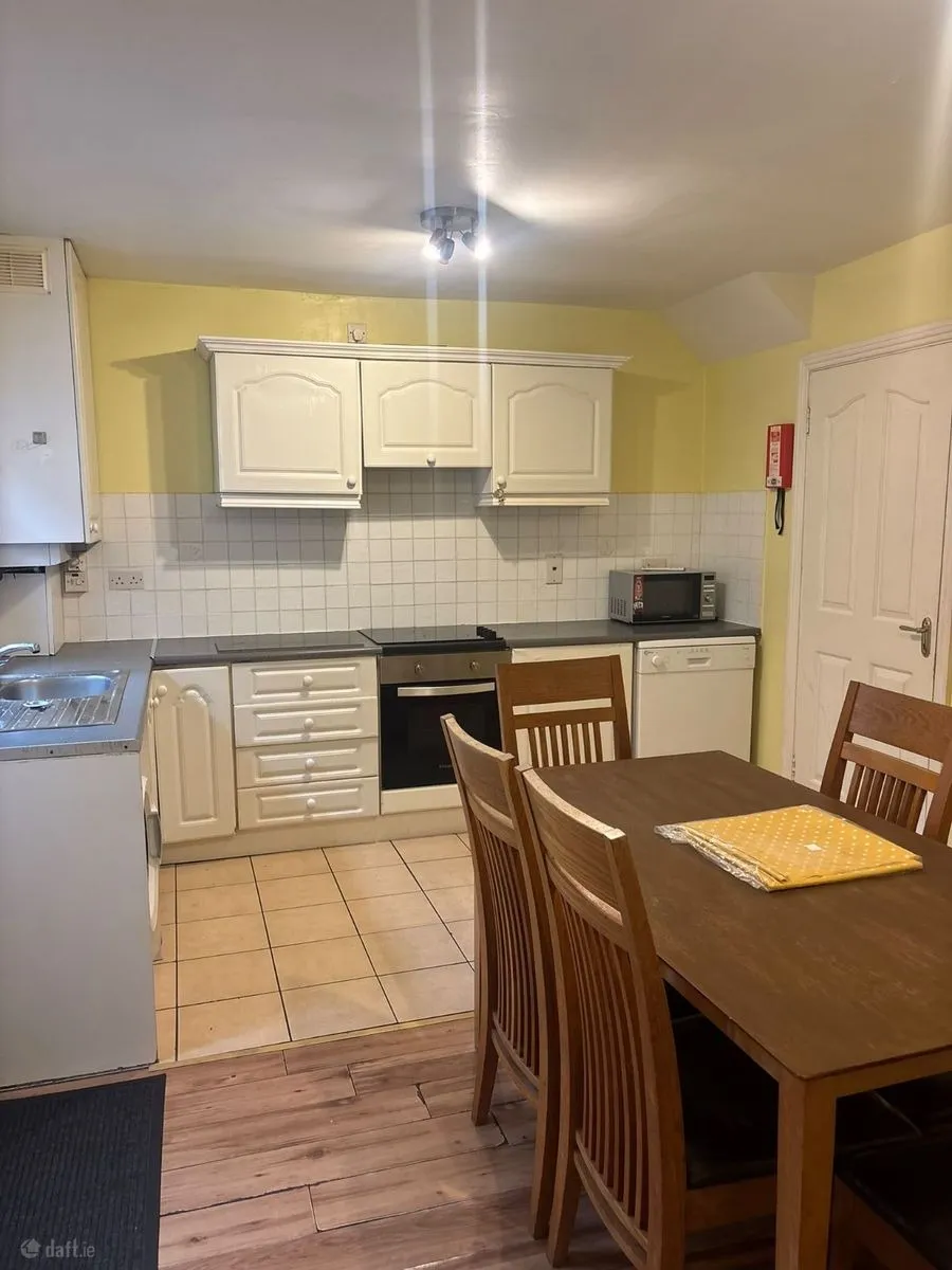 Kitchen with white cabinets, countertop, built-in oven, sink, microwave and a wooden dining table with four chairs