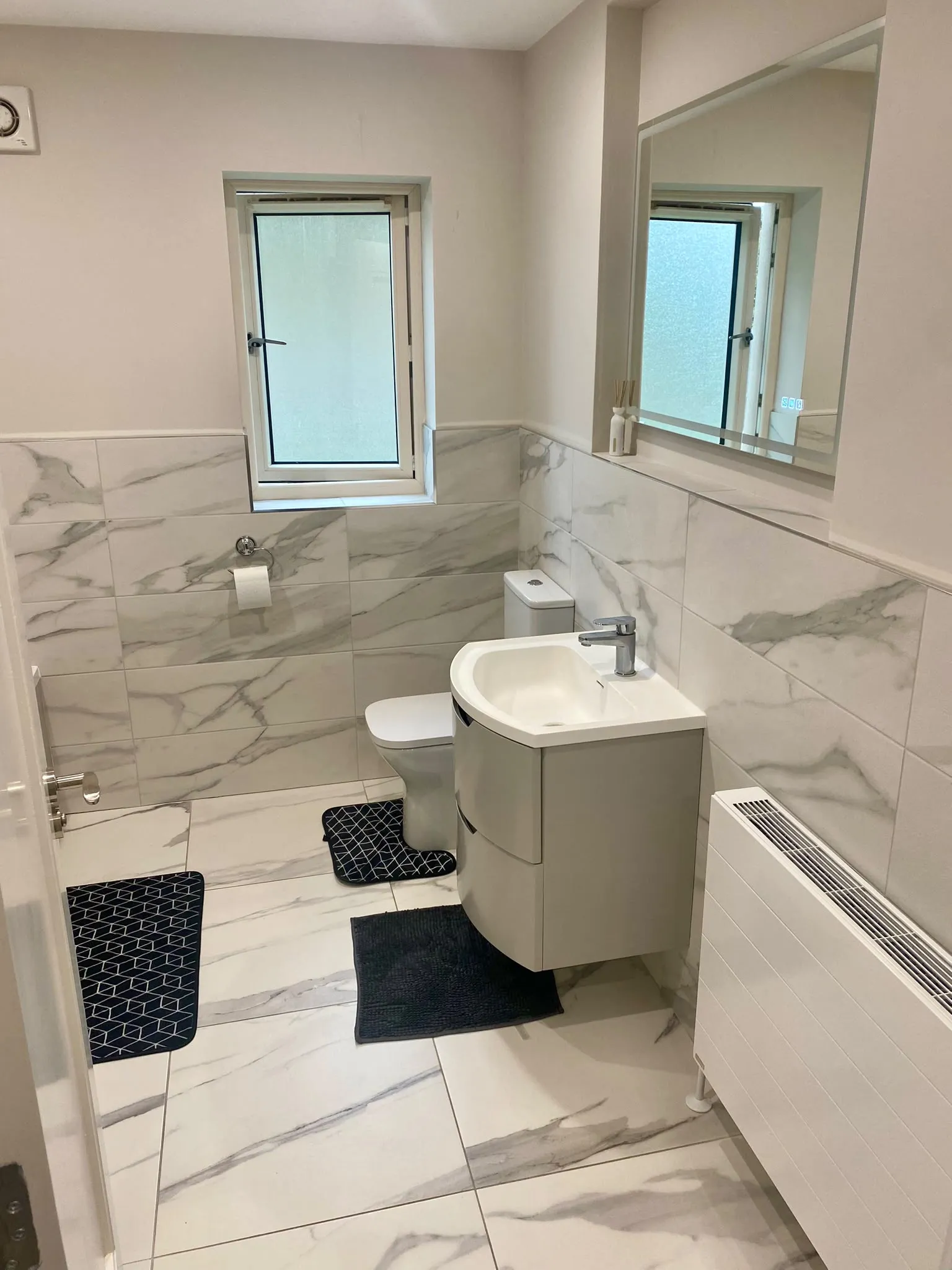 Bathroom with a sink and vanity, toilet, wall mirror, frosted window, and tiled walls and floor